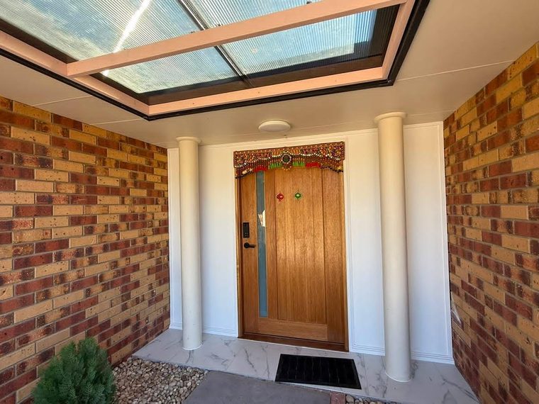 Same home's front porch finished with marble-look tiling, rendered columns, a timber door and a skylight