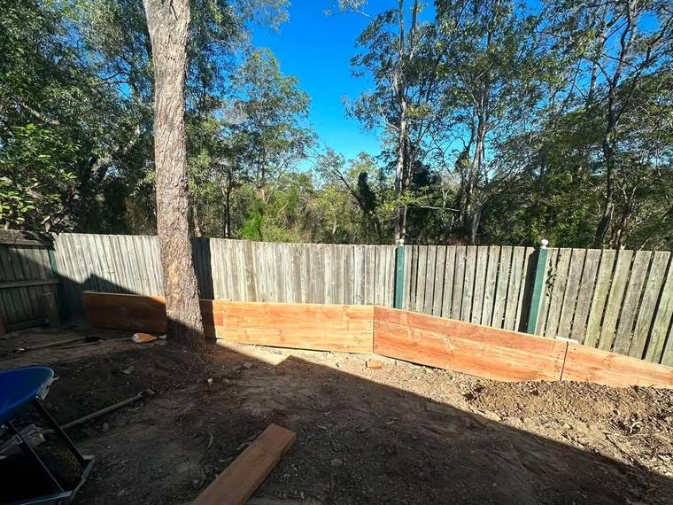Treated timber sleeper retaining wall under construction along a boundary fence